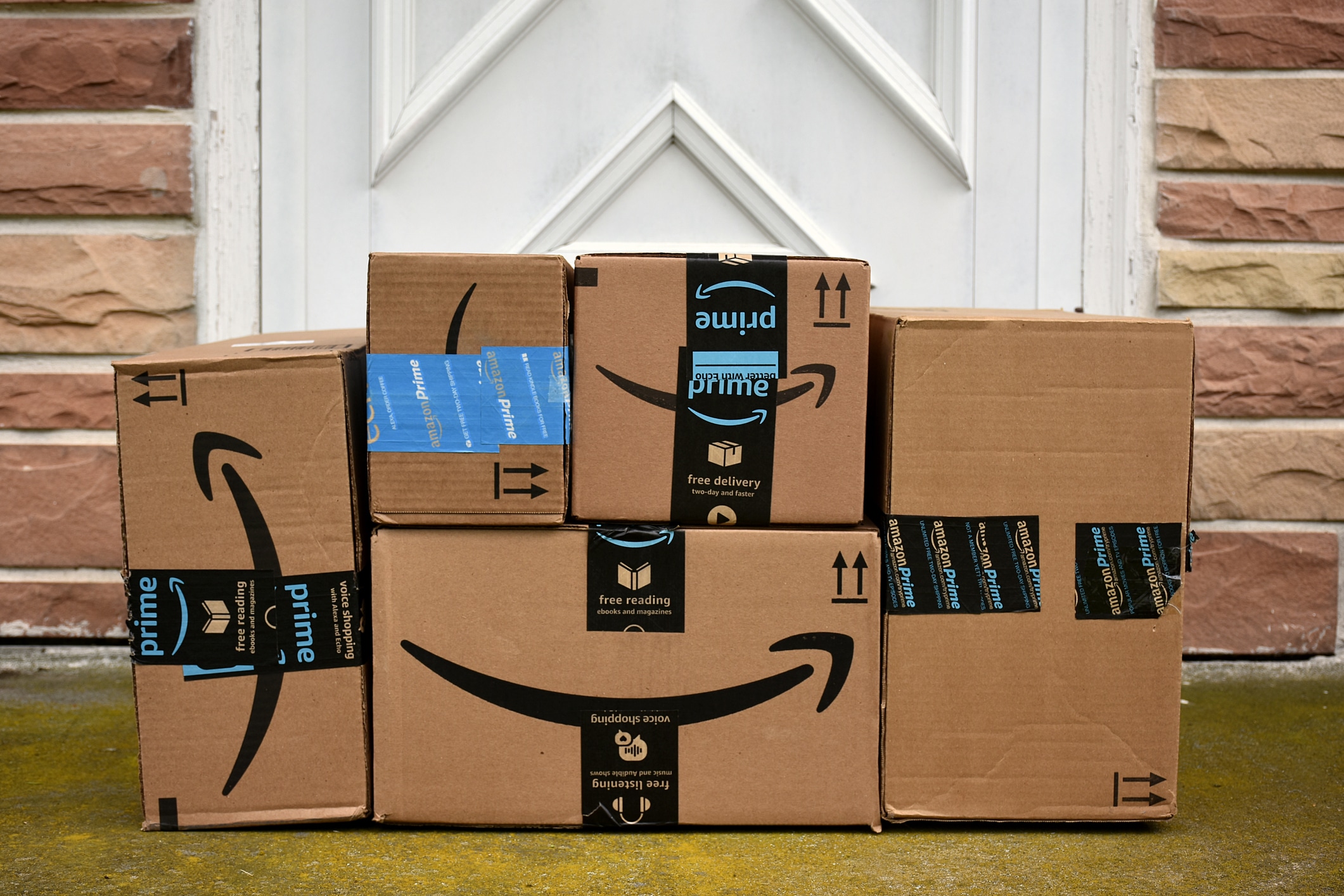 A pile of Amazon shopping boxes piled up on the doorstep of an old stone and brick house.