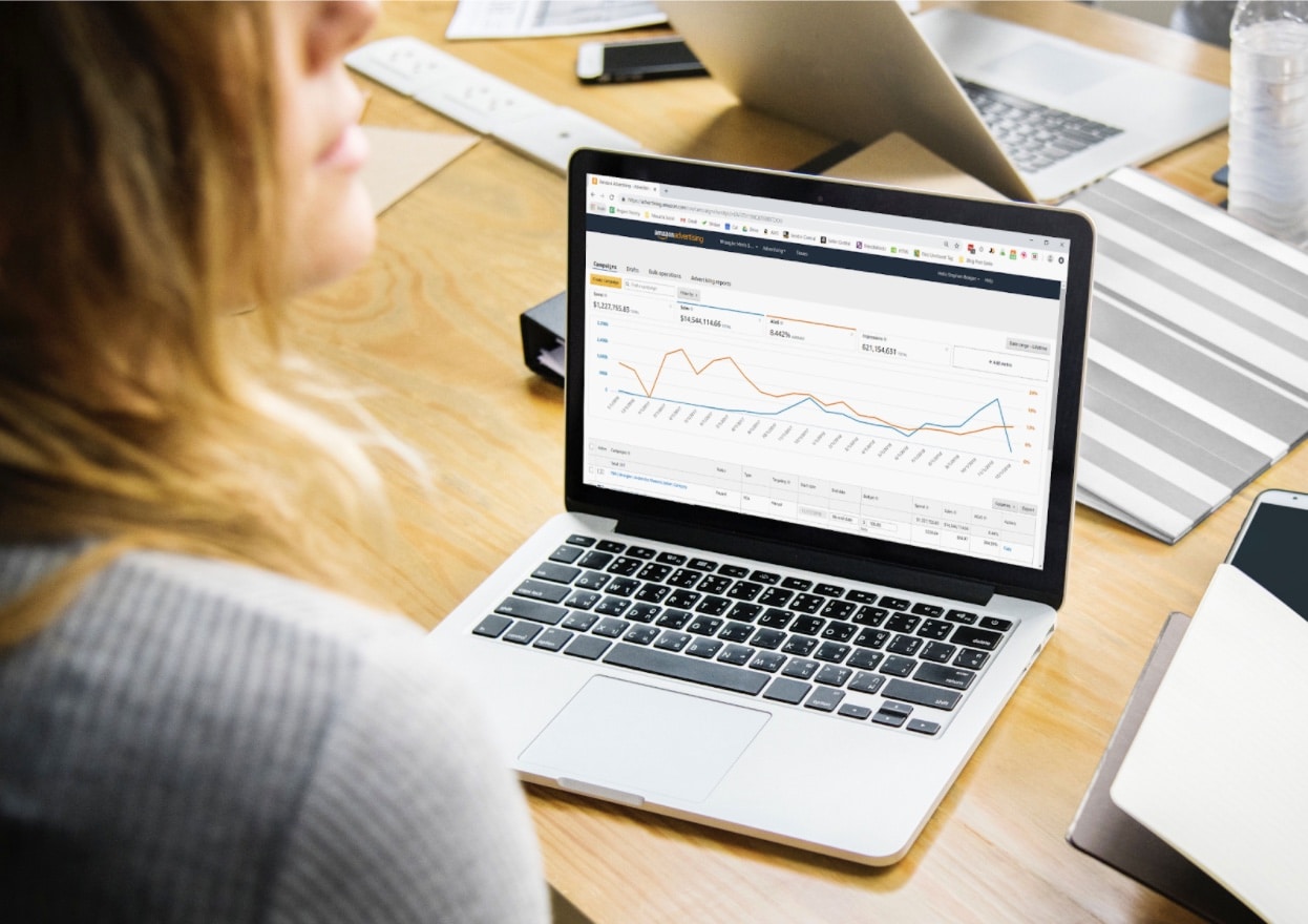 A woman sitting at a laptop looking at Amazon Ads insights on the screen