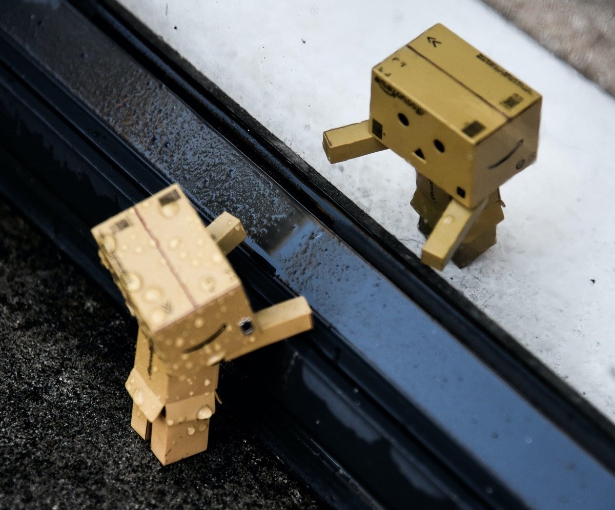 Two little robots made from Amazon Ads are at a roadside kerb. One is helping the other up.